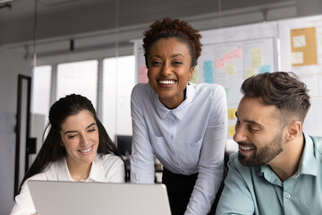 Cheerful young businesswoman standing at work desk between two apprentices