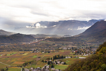 Scenic aerial panorama view of French alps in Savoie region, rocky mountain with vineyard and village, cloudy drama sky during autumn