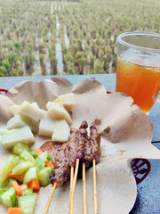 Authentic Sate Ayam Served Outdoors on a Rustic Table Against a Harvested Paddy Field View