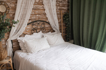 Details of bright elegant interior in cozy bedroom. Wicker side table with vase and flowers next to comfortable bed with white linen bedding. 