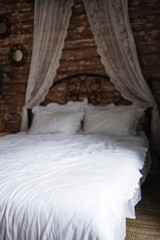 Details of bright elegant interior in cozy bedroom. Wicker side table with vase and flowers next to comfortable bed with white linen bedding. 