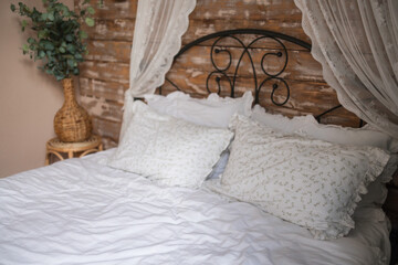 Details of bright elegant interior in cozy bedroom. Wicker side table with vase and flowers next to comfortable bed with white linen bedding. 