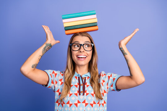 Young woman balances a colorful stack of book on her head in a playful studio shot