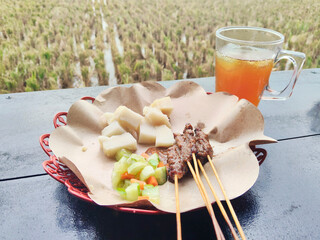 Traditional Indonesian Chicken Satay with Rice Cakes and Ice Tea in Rural Restaurant