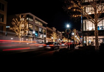 Cars create red light trails on a dark city street lined with trees covered in golden lights