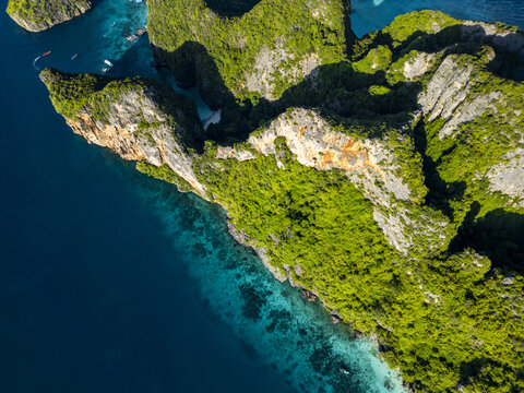 Aerial view of vibrant green foliage contrasts with the rugged cliffs and turquoise waters of Phi Phi Islands, Krabi, Thailand.
