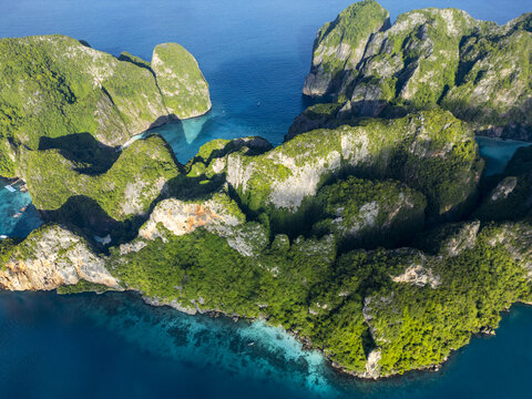 Aerial view of towering limestone cliffs draped in emerald vegetation meeting the turquoise waters of Maya Bay, a tropical paradise., phi phi, krabi, Thailand.