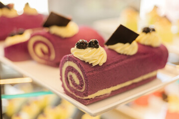 Colorful roll cakes featuring a vibrant purple exterior and creamy filling sit elegantly on a display shelf in a dessert shop, attracting customers with their delightful look