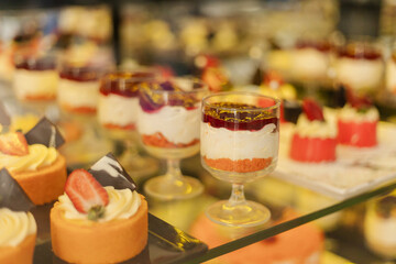 A tempting array of desserts showcases vibrant cakes and creamy layers topped with fruits in a pastry shop. The delicious treats are arranged neatly, inviting customers to indulge