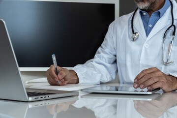 Dedicated doctor in a clinic setting, working with a tablet and laptop, symbolizing modern medical practice