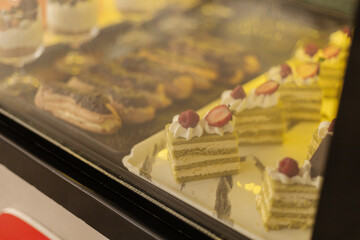 Delicious layered cakes and pastries are beautifully arranged in a bakery display case. Each treat features unique decorations, attracting customers with their sweet appeal