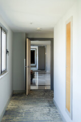 A long hallway shows several open doors on both sides. Natural light fills the space, highlighting the clean lines and modern design. The floor appears sleek and polished