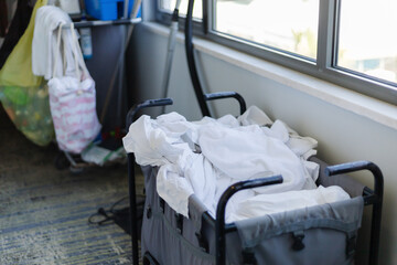 Housekeeping staff organizes clean white linens in a cart within a hotel room. The room features large windows letting in natural light, creating a neat environment