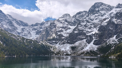 Fototapeta premium Mountain landscape featuring a serene lake surrounded by jagged, snow-capped peaks. 