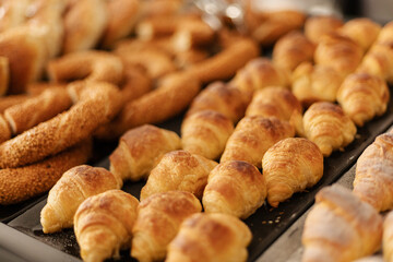A variety of freshly baked pastries are arranged on a tray in a bakery. Soft croissants and bread rolls glisten under the warm light, inviting customers to enjoy a morning treat