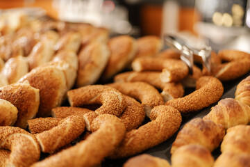 A selection of warm, golden pastries is arranged on a table in a bakery. The aroma fills the air as customers are welcomed to choose their favorites during morning hours
