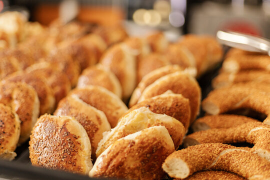 A variety of freshly baked bread rolls and pastries are arranged neatly on a tray in a warm bakery setting. Customers explore the delicious options