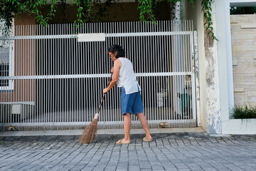 woman doing daily routines, sweeping the front garden using broomstick