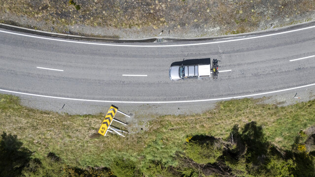 Aerial view of a silver van passing a storm felled road warning sign, contrasted against the lush greenery, Hanmer Springs, Canterbury Region, New Zealand.