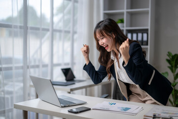 Excited businesswoman celebrating success while working on laptop in office