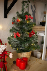 Decorated small Christmas tree with red ribbons and fairy lights inside a woven pot. Festive home decor for new year celebration.