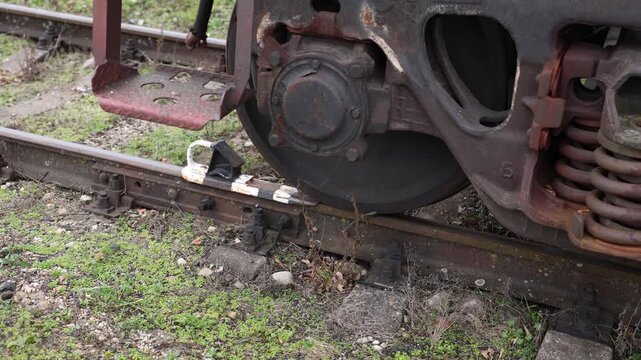 Close-up of a freight train wheel secured in place by a white rail stop block on an overgrown and weathered section of railway track