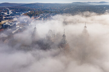 Aerial view of the imposing Schloss Johannisburg castle partially shrouded in ethereal mist, its spires piercing the fog, Aschaffenburg, Bayern, Germany.