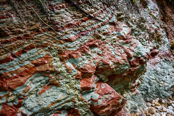 Vibrant layered clay outcrop, showcasing striking red and teal strata. Natural erosion reveals...