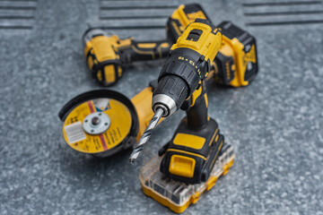 Cordless drill with a metal drill bit, angle grinder and impact wrench on a steel surface. Concept of construction, workshop tools, industrial work, maintenance and professional craftsmanship.
