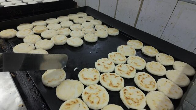 Large batch of traditional arepas cooking on a griddle in a restaurant
