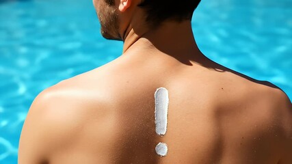 Close up of a man's back with white sunscreen in the shape of an exclamation mark against a bright blue blurred water background indicating sun