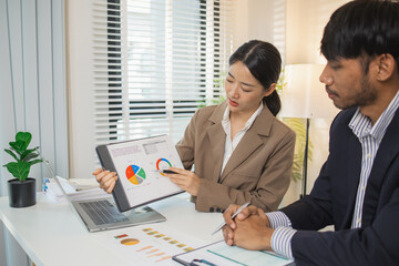 Two business professionals are discussing financial charts and reports in a modern office. They collaborate, share ideas, and analyze data together, highlighting teamwork and strategy.