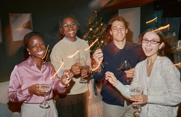 Group of young adult multiethnic friends celebrating together holding sparklers and drinks smiling...