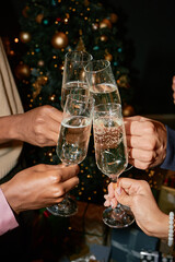 Diverse group of young adult hands clinking champagne glasses in front of decorated Christmas tree, celebrating festive occasion with sparkling wine