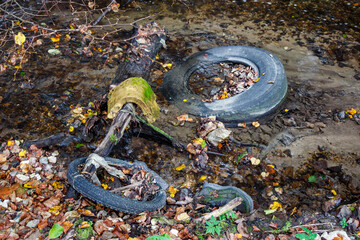 An unsightly mess of discarded tires, a boot, and other rubbish litters a shallow stream,...