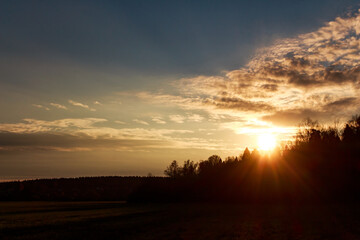 Stunning sunset over silhouetted trees, with golden rays bursting through the cloudy horizon. A serene and beautiful natural twilight vista