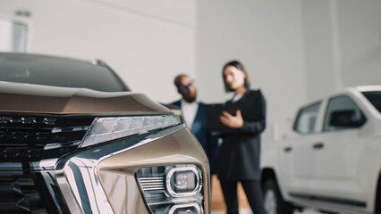 A close-up of the front grille of a modern car with buyers and a salesperson discussing...