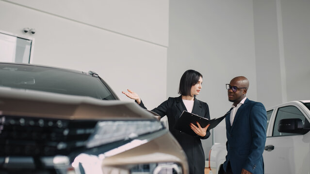 African American man engaging with a female car salesperson in a dealership, discussing vehicle features and options, showcasing the car buying experience and customer service