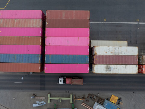 Aerial view of vibrant pink, brown, blue and white cargo containers stacked high near a road with a truck, Berlin, Germany.