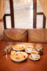 Relaxing tea time in a cozy lounge area after sauna session, with cups of tea, teapots and desserts on a wooden table near window in warm interior.