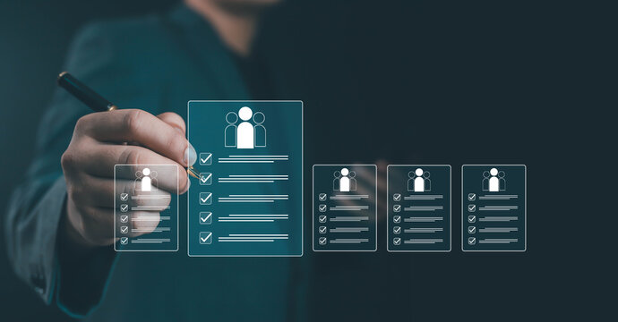 Businessman selecting digital checklist with user profile icons on virtual screen, symbolizing employee management, HR technology, recruitment system, and performance evaluation. - Powered by Adobe