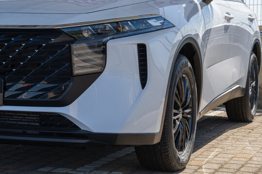 Front lower section of modern white Chinese  SUV Venucia, highlighting its headlight design, black grille, and alloy wheels. Hyundai car dealership is in Adygea. Krasnodar, Russia, September 15, 2025