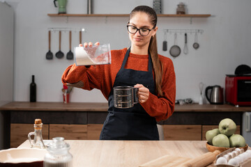 Portrait of woman wearing apron cooking apple pie enjoy making clean food sifting flour in kitchen at home. baking, cookies and dessert.