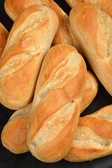 A close-up, vertical shot shows a textured pile of freshly baked, golden-brown bread rolls resting on a dark surface