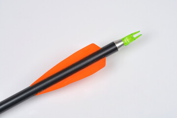 A close-up shot captures the black shaft, orange fletching feathers, and fluorescent green plastic nock of an arrow on a plain white background