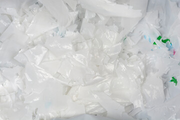A high-angle, full-frame close-up shows a large pile of shiny, brittle, and partially degraded white and translucent plastic bag pieces, highlighting plastic pollution