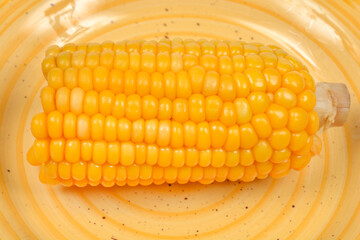 A close-up, horizontal view showcases the shiny, bright yellow kernels of a half-cob of cooked corn resting on a textured yellow plate