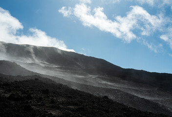 Close-up of the desolate, rocky slope of an active volcano (Mount Etna), with ash and steam carried by the wind under a blue sky, Sicily, Italy.