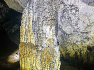 Detailed view of a stalagmite in a natural cave, showing rich mineral deposits and layered limestone texture illuminated by cave light.