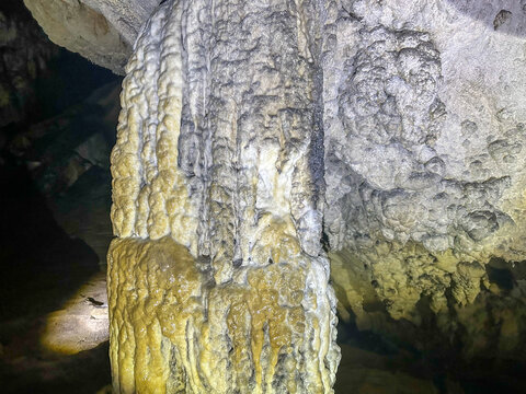 Detailed view of a stalagmite in a natural cave, showing rich mineral deposits and layered limestone texture illuminated by cave light.